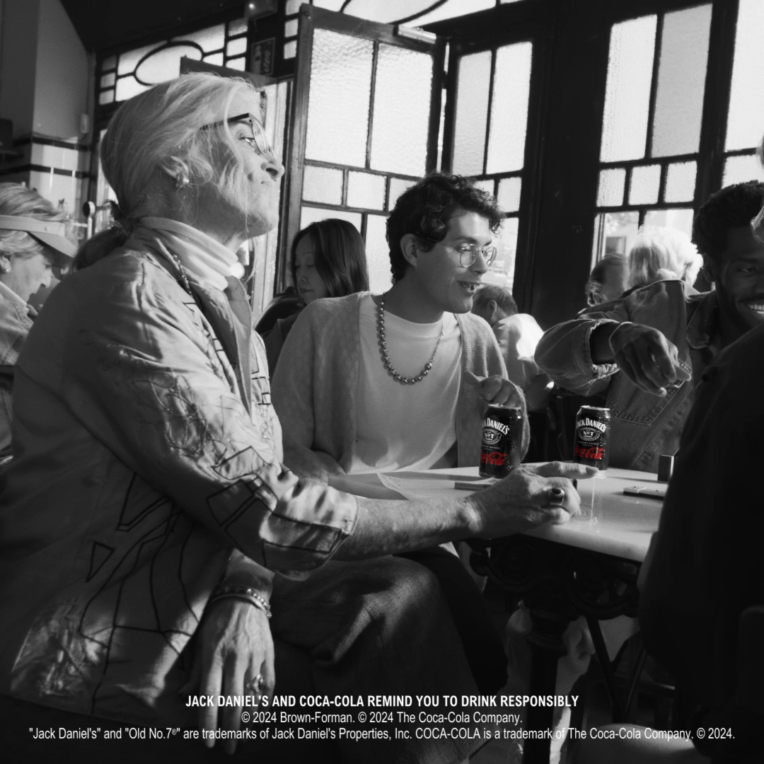 Ljudi sede oko stola igrajući društvene igre, sa limenkama „Jack Daniel’s & Coca-Cola“ ispred sebe, praćeno krupnim kadrom limenke u fokusiranom prikazu sa kapljicama vode.
