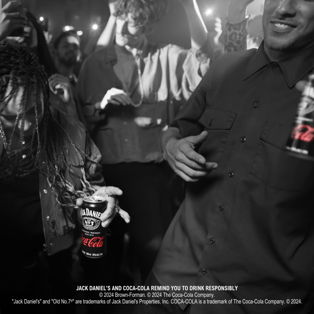 Dorë duke mbajtur një kanaçe Jack Daniel’s dhe Coca-Cola me sfond dritash të turbullta dhe tekstin “Born Ready” në pjesën e poshtme.